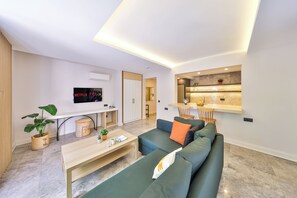 A modern living room with a sofa, coffee table, and a TV. There is a kitchen area with a countertop and a plant. - Sole Suites (Kaş)