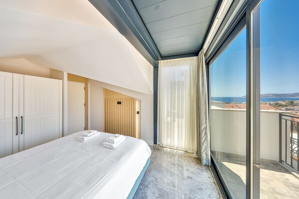 A modern hotel room with a large bed, a wardrobe, a wooden panel wall, and a balcony with a view. - Sole Suites (Kaş)