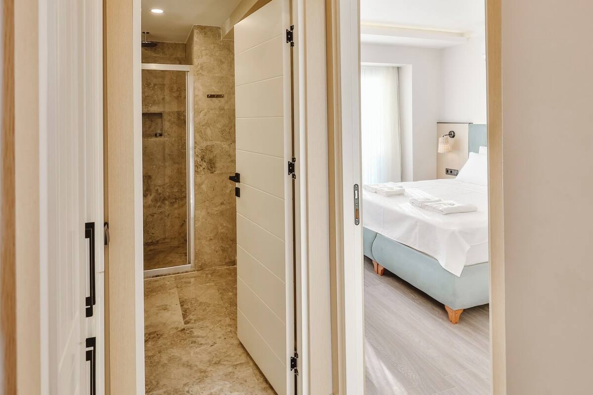 Hotellihuone, jossa on sänky, kylpyhuone suihkulla sekä käytävä, joka johtaa toiseen huoneeseen.