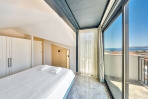 A modern hotel room with a large bed, a wardrobe, a wooden panel wall, and a balcony with a view. - Sole Suites (Kaş)