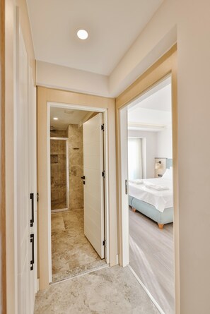 A hotel room with a bed, a bathroom with a shower, and a hallway leading to another room. - Sole Suites (Kaş)