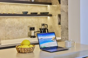 A laptop on a kitchen counter with a basket of lemons, a mug, and a coffee maker in the background. - Sole Suites (Kaş)