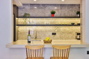A modern kitchen with a marble backsplash, a built-in sink, and two wooden chairs at the counter. - Sole Suites (Kaş)