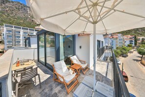 Une terrasse sur le toit avec une balustrade en verre, une table avec une bouteille et des verres, deux fauteuils de jardin en bois et un grand parasol.