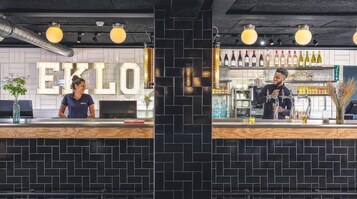 A bar area with a black tiled wall, a large illuminated sign reading "EXLO", and a variety of bottles on shelves.