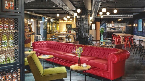 Un interior moderno con un sofá de cuero rojo, un sillón verde y mesas redondas.