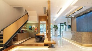 A modern hotel lobby with a wooden reception desk, a seating area with a table and chairs, and a staircase leading to another level. - Yitel Hotel Shanghai Hongqiao Airport Lianming Road Branch (Shanghai)