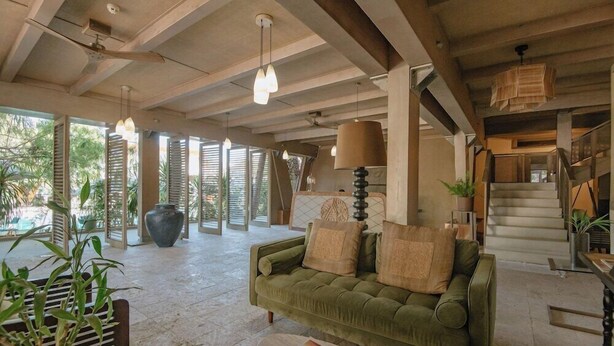 A spacious living area with a green sofa, a coffee table, and a large vase. There is a staircase to the right and a view of the outdoors through large windows. - Asmara Urban Resort and Lifestyle Village Powered by Aston (Cebu City)
