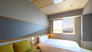 Une chambre d’hôtel moderne avec un grand lit, un banc agrémenté de coussins, une petite table et une fenêtre donnant sur un paysage urbain.