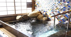 Un bain de source thermale en pierre, avec un mur carrelé et un plancher en bois.