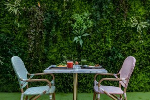 Een terras met een tafel en twee stoelen, omringd door een weelderige groene haag.