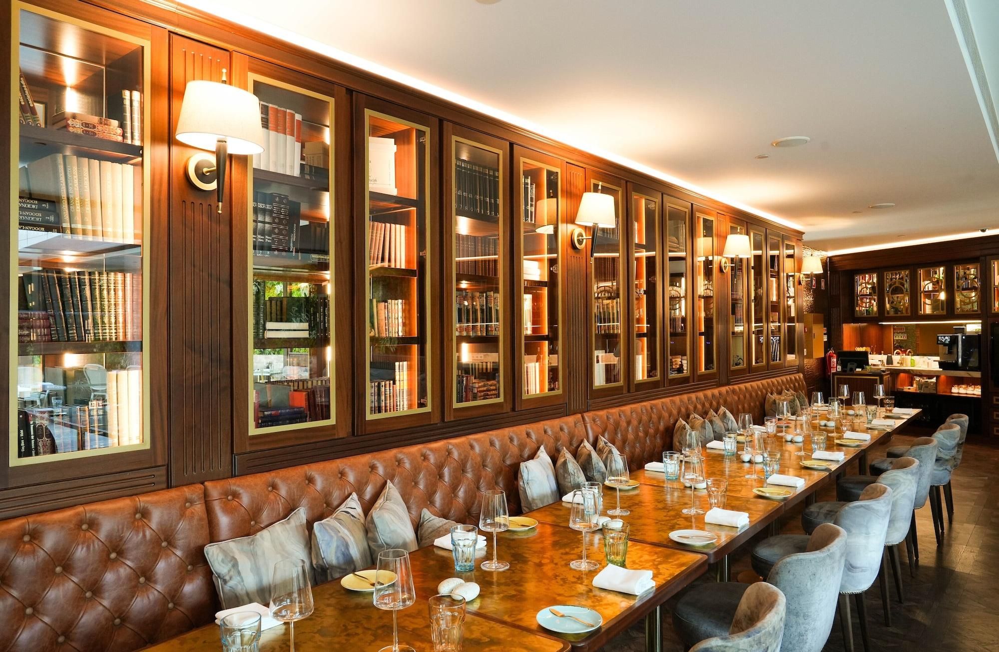 A long dining table with chairs, a leather bench, and bookshelves with glass doors.