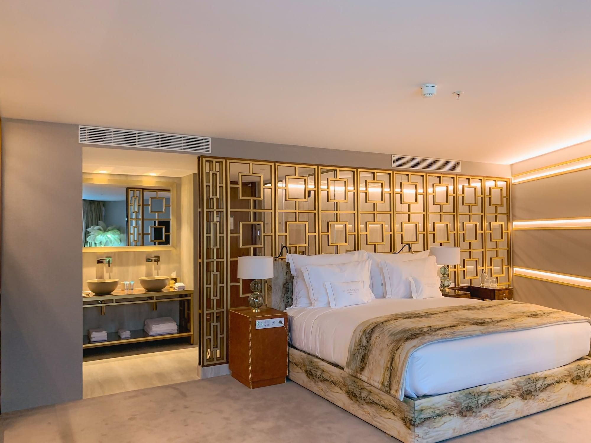 Una habitación de hotel moderna con una cama grande, un baño con tocador y un panel decorativo en la pared.