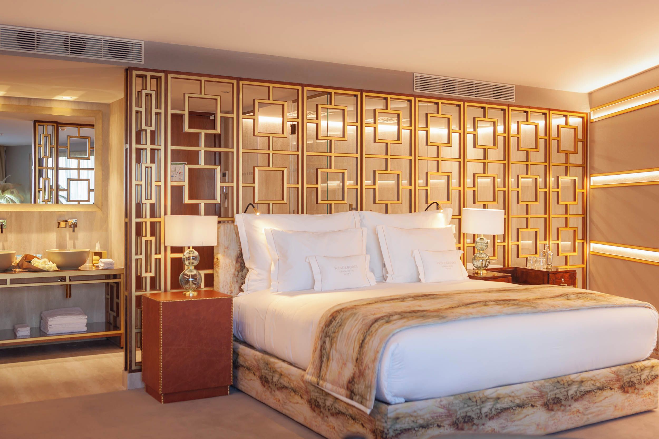 Habitación de hotel con una cama grande, una mesita de noche con lámpara, un tocador con espejo y un panel decorativo en la pared.