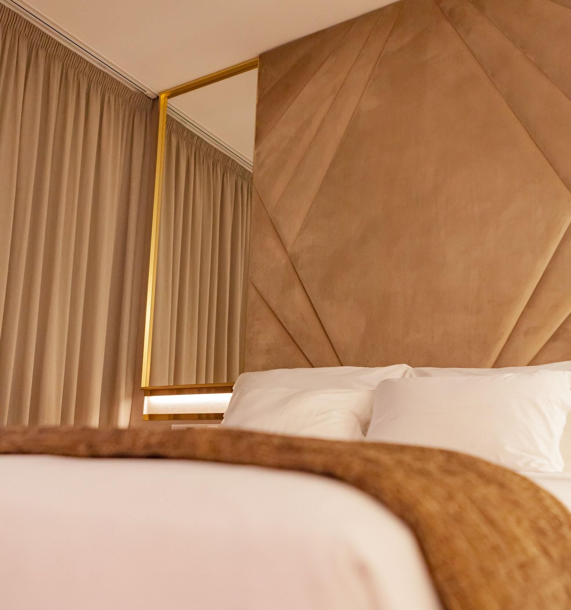 A hotel room with a bed, a large mirror, and curtains.