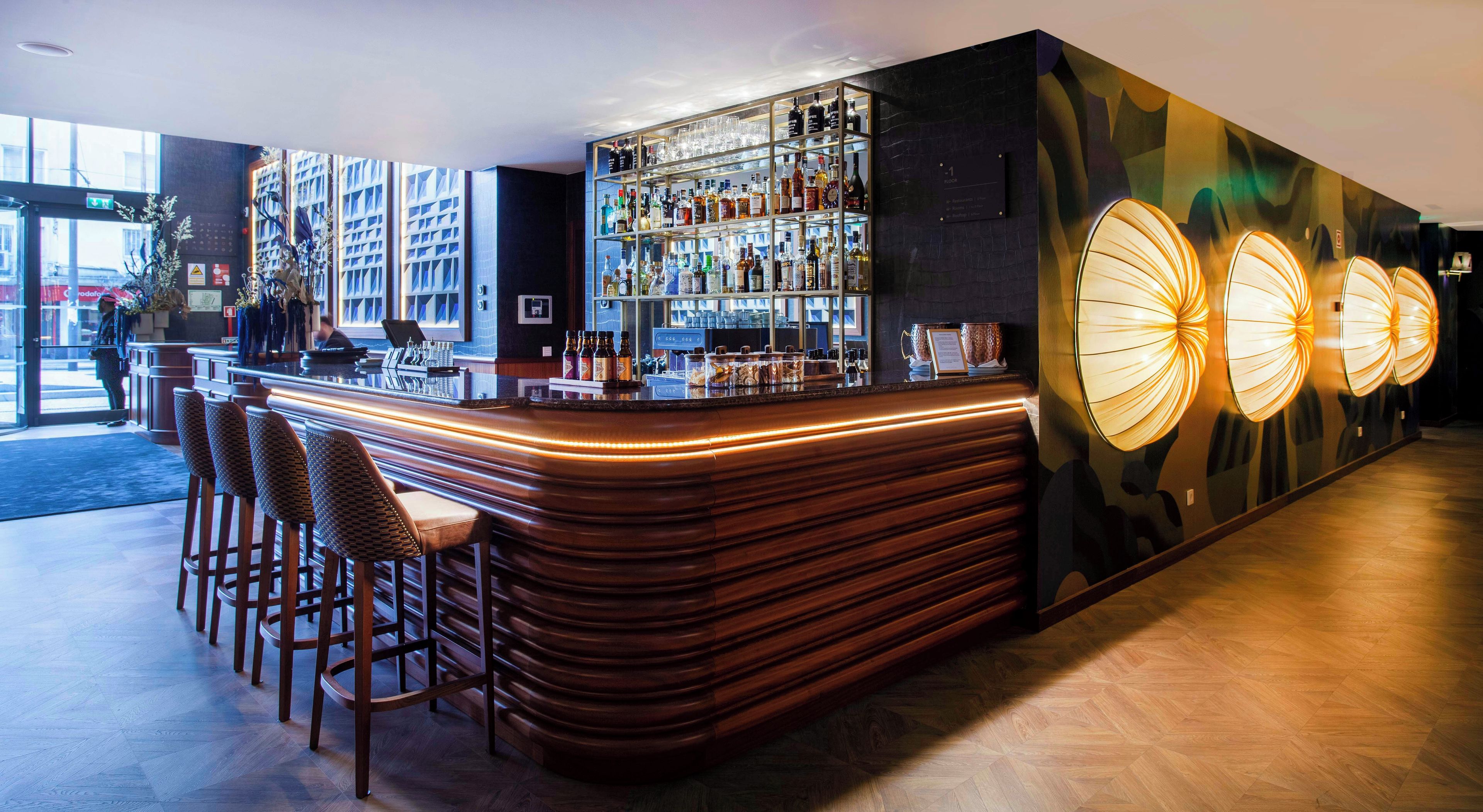 Un espace bar doté d’un comptoir incurvé, de tabourets de bar et d’une étagère fixée au mur où sont exposées des bouteilles.