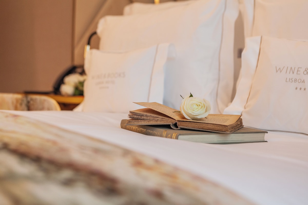 Ein Bett mit einem Buch, einer Rose und weißen Taschen mit Text.