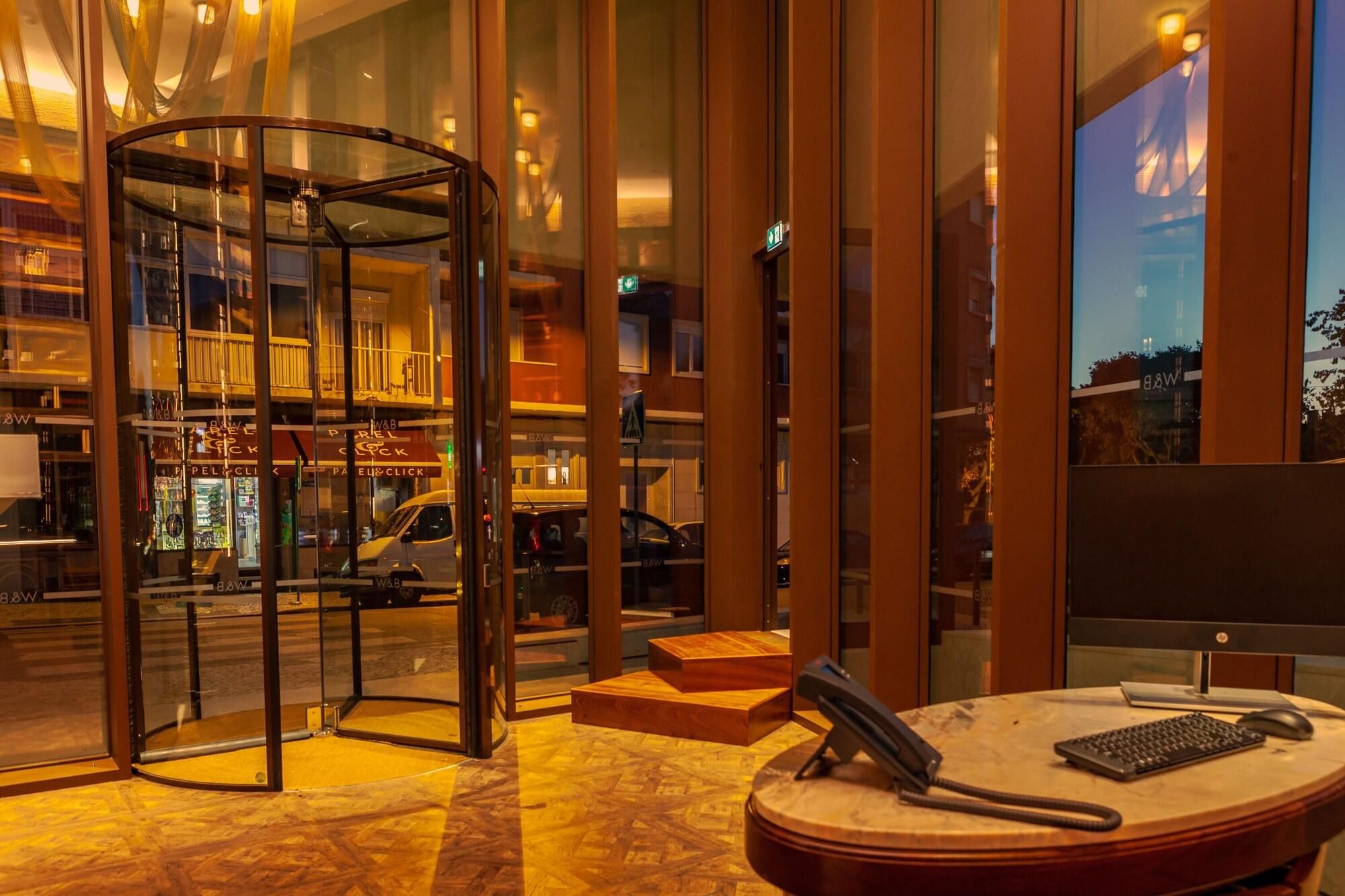Um saguão de hotel com uma porta giratória, balcão de recepção e vista para a rua.