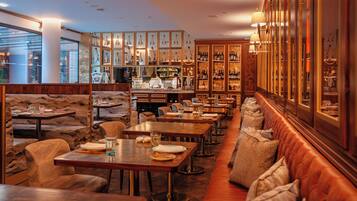 A restaurant with wooden tables, cushioned booths, and a bar area with wine bottles.