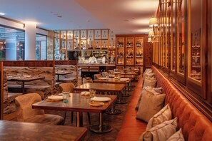 Een restaurant met houten tafels, comfortabele zithoeken en een bar met wijnflessen.