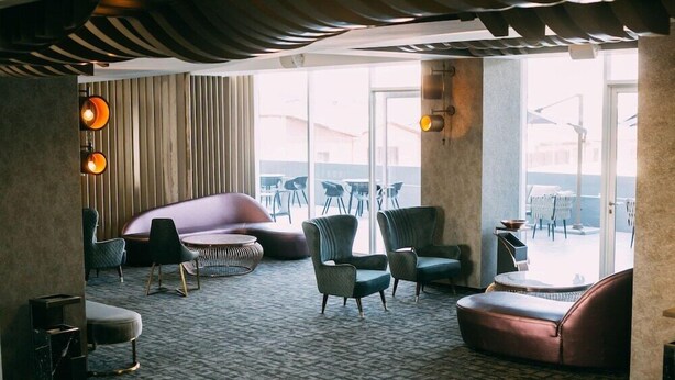 Un espace de détente moderne, doté d’un tapis à motifs, de meubles contemporains et de grandes fenêtres offrant une vue sur l’extérieur.