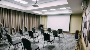 Une salle de conférence avec des rangées de chaises, un projecteur et un écran.