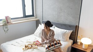 A bed with a white comforter, a tray with snacks and a glass of wine, a bedside table with a lamp, and a window with a plant and books. - Chambers Kuala Lumpur by Five Senses (Kuala Lumpur)