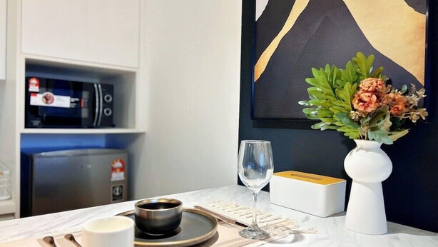 A modern kitchen with a microwave, a coffee machine, and a white cabinet. There is a vase with flowers on the counter. - Chambers Kuala Lumpur by Five Senses (Kuala Lumpur)