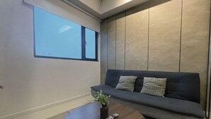 A modern living room with a dark grey sofa, a small coffee table, and a window with blinds. - Chambers Kuala Lumpur by Five Senses (Kuala Lumpur)