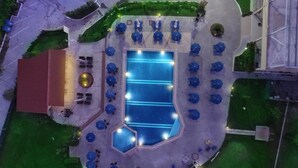 An aerial view of a swimming pool area with multiple lounge chairs and umbrellas, surrounded by a landscaped garden. - Kornilios Palace Thessaloniki (Chalkidona)