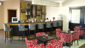 A bar area with a counter and multiple bar stools, surrounded by red and black patterned chairs and tables. - Kornilios Palace Thessaloniki (Chalkidona)