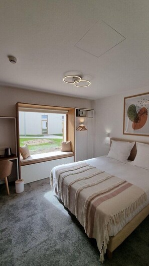 Een moderne slaapkamer met een groot bed, een vensterbank, een bureau en uitzicht op de omgeving.