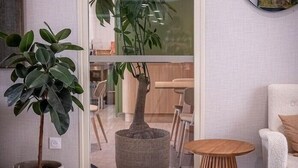 Ein modernes Wohnzimmer mit einer großen Küstpflanze, einem runden Holztisch und einem weißen Sessel.