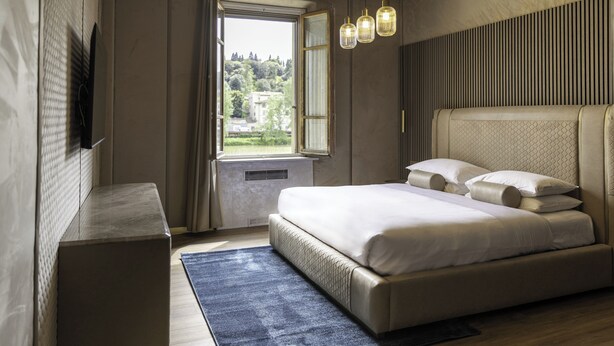 A bedroom with a large bed, a window with curtains, a bedside table, and a hanging light fixture. - Le Reve De Naim (Florence)