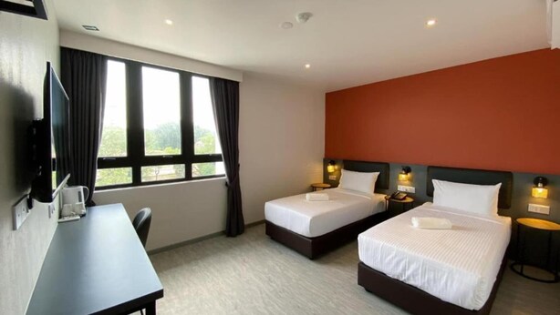 A hotel room with two beds, a desk, a TV, and a window with curtains. - Woco Hotel Kinrara (Puchong)