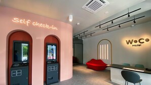A self-check-in kiosk, a reception desk, and a WOC Hotel sign in a modern lobby. - Woco Hotel Kinrara (Puchong)