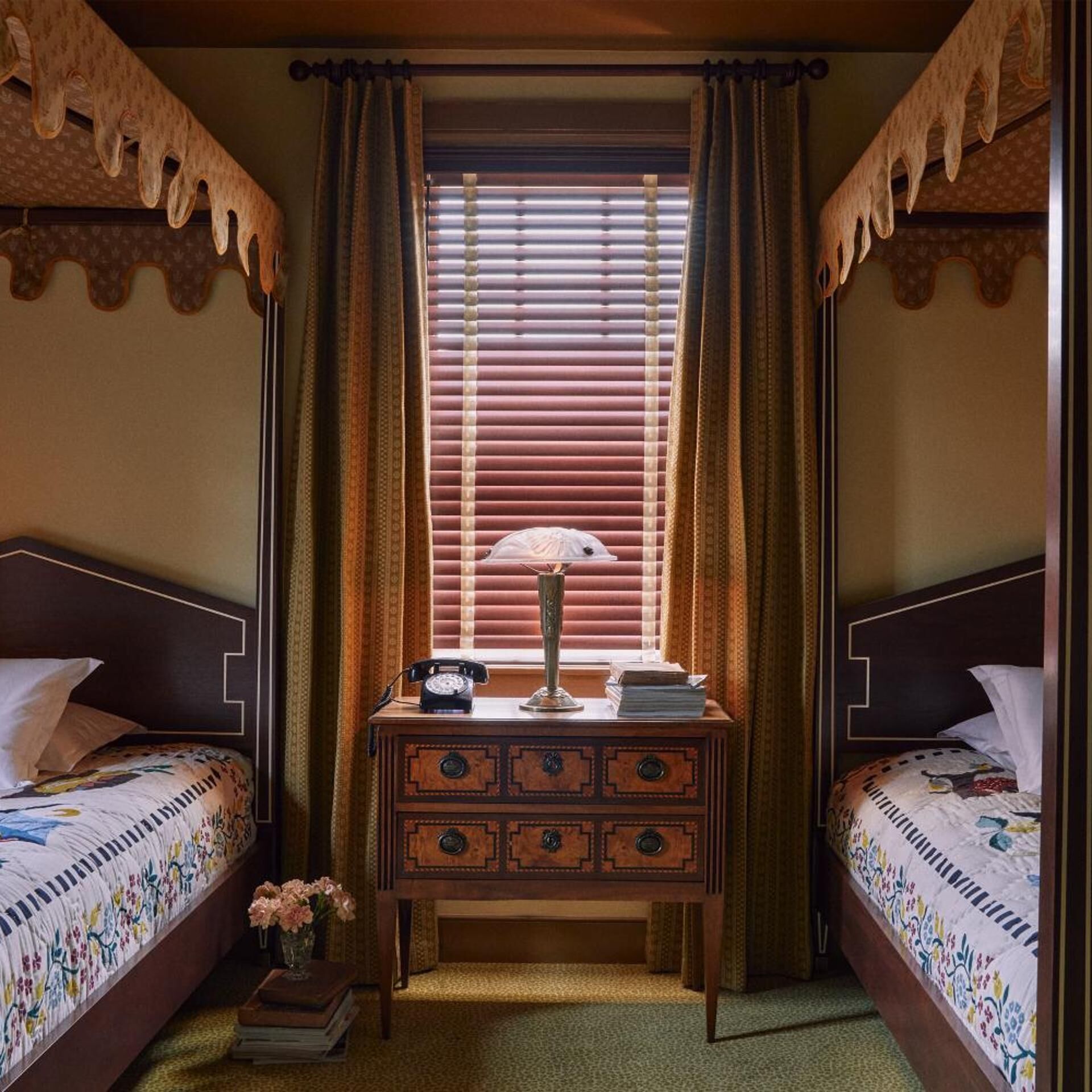 Ein Zimmer mit zwei Betten, einem Schreibtisch mit Lampe und einem Fenster mit Jalousien.