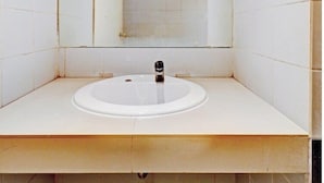 Een badkamer met een wit wastafel, een spiegel en een deur naar een andere kamer.