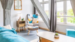 A room with a sloped ceiling, a wooden chair with a colorful cushion, a small wooden side table, a mirror, and a window with curtains. - Das königliche Quartier by Interhome (Mirow)
