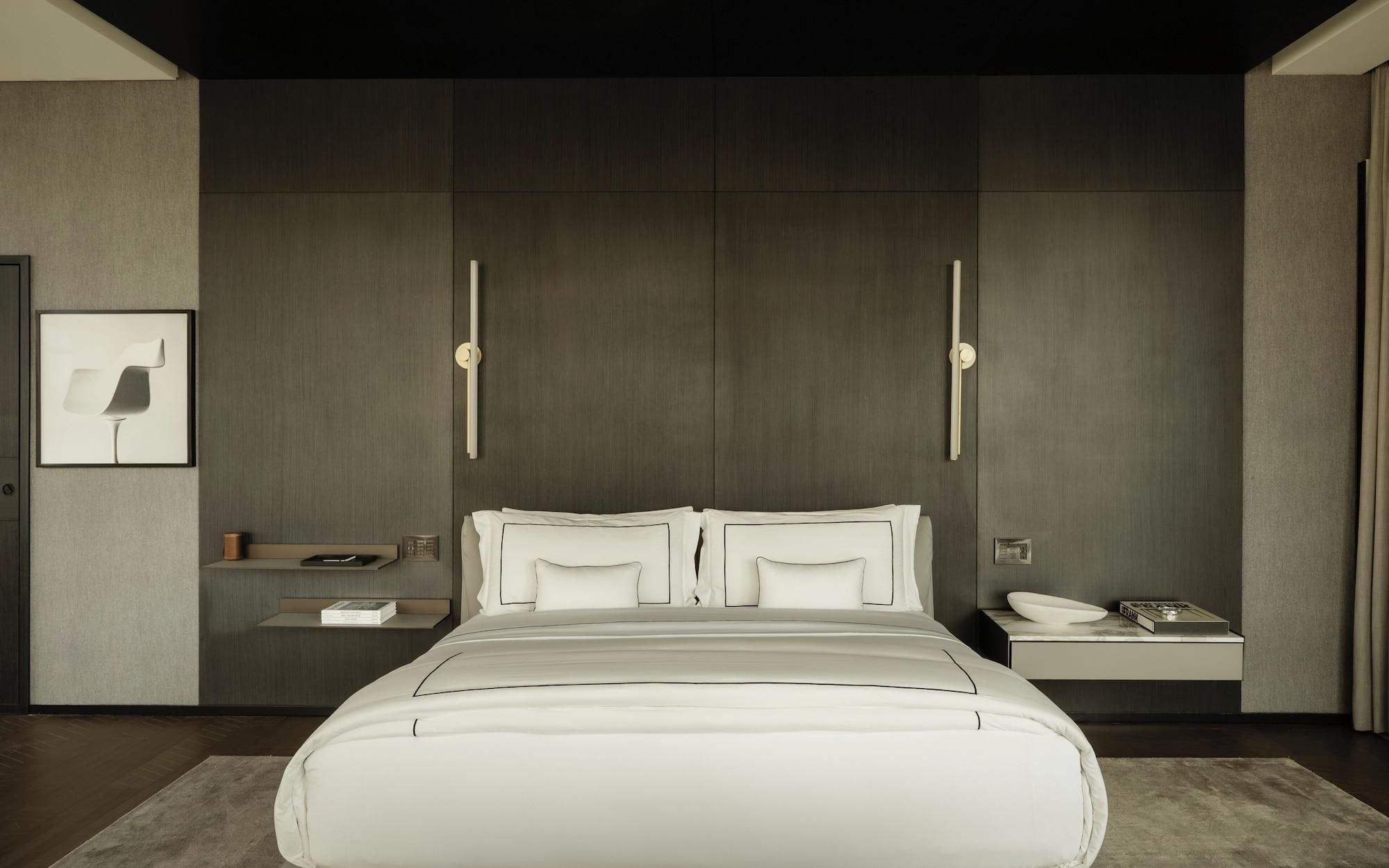 Une chambre à coucher moderne avec un grand lit, des tables de chevet, une petite table et un tableau encadré au mur.