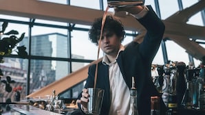 A bartender pouring a drink at a bar with a modern interior and large windows. - Hotel Alexander (Mexico City)