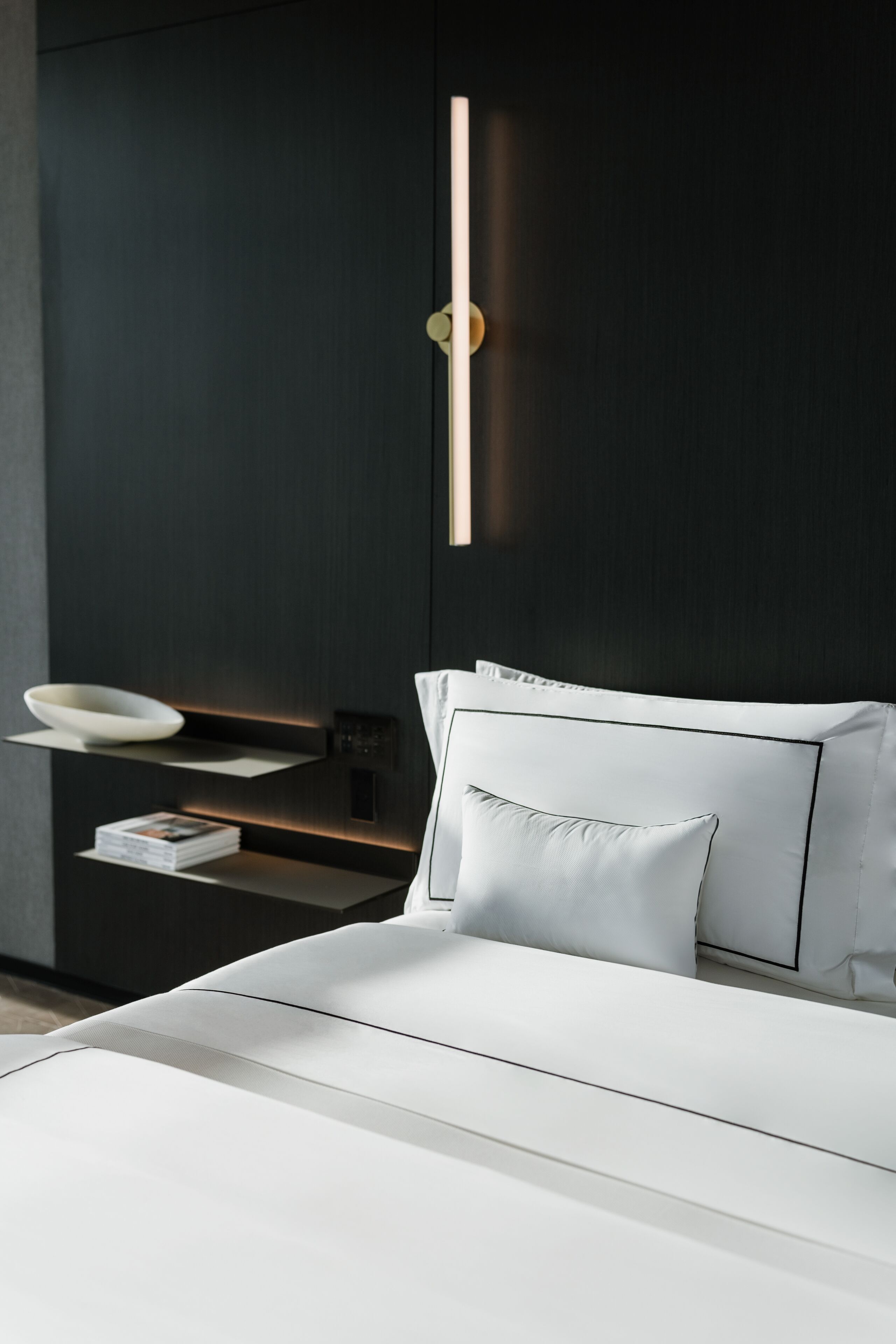 A modern bedroom with a bed, bedside tables, and a wall-mounted light fixture.