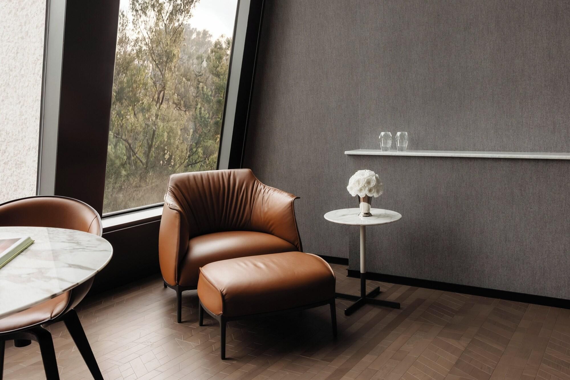 Een moderne kamer met een lederen fauteuil, een klein rond tafeltje met een vaas, en een plank met glazen.