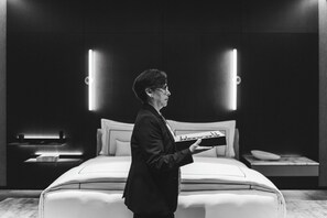A person standing in a modern bedroom with a bed, nightstands, and illuminated wall panels. - Hotel Alexander (Mexico City)