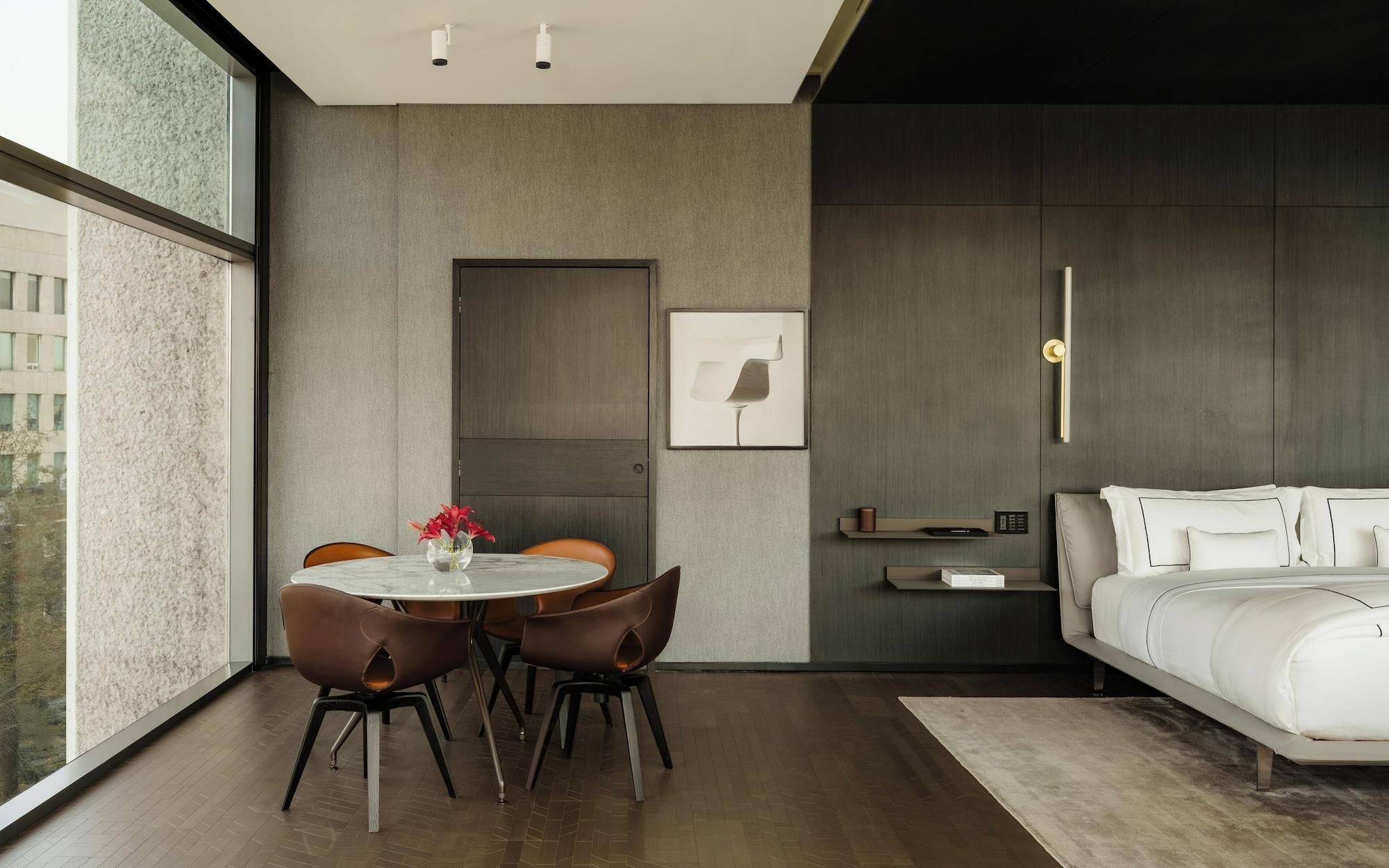 A modern bedroom with a bed, a bedside table, a nightstand, and a wall-mounted light fixture.