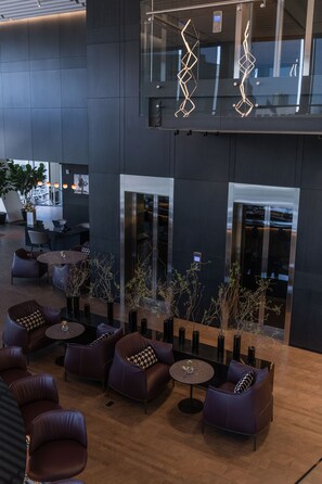 A modern lobby with leather seating, a glass elevator, and a view of the interior space. - Hotel Alexander (Mexico City)
