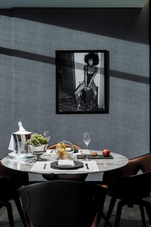 A dining table with a white marble top, surrounded by black chairs, set with a silver pitcher, a bowl of fruit, and a glass of water. - Hotel Alexander (Mexico City)
