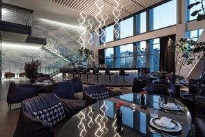 A modern hotel lobby with a curved glass table, leather seating, a bar area, and a staircase. - Hotel Alexander (Mexico City)