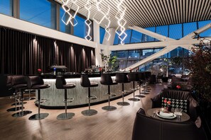 A modern bar area with a central bar, multiple stools, and a seating area with a sofa and table. - Hotel Alexander (Mexico City)
