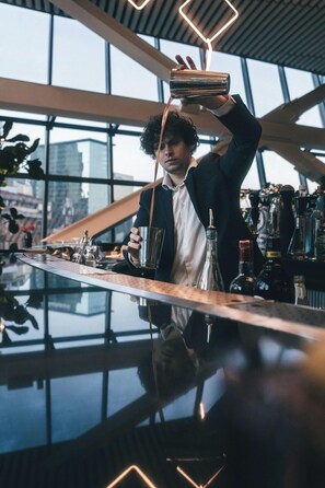 A bartender pouring a drink at a bar with a modern interior and large windows. - Hotel Alexander (Mexico City)